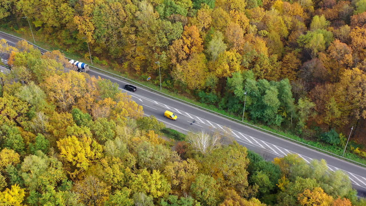Highway with cars with colorful trees from both sides. Cars moving on the road among forest in fall. Treetops and asphalt road with automobiles. Top aerial view.
