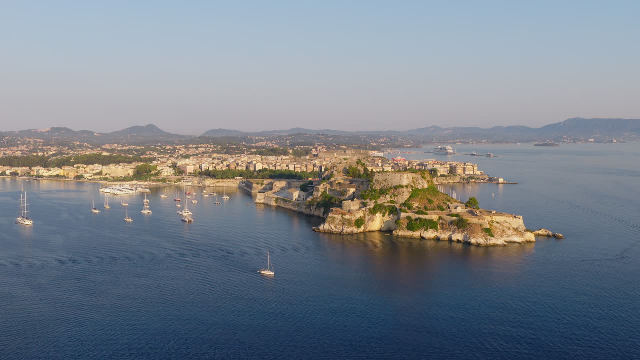 Aerial view of luxury yachts sailing in front of Corfu Old Town and marina with ancient fortress at sunrise, Greece
