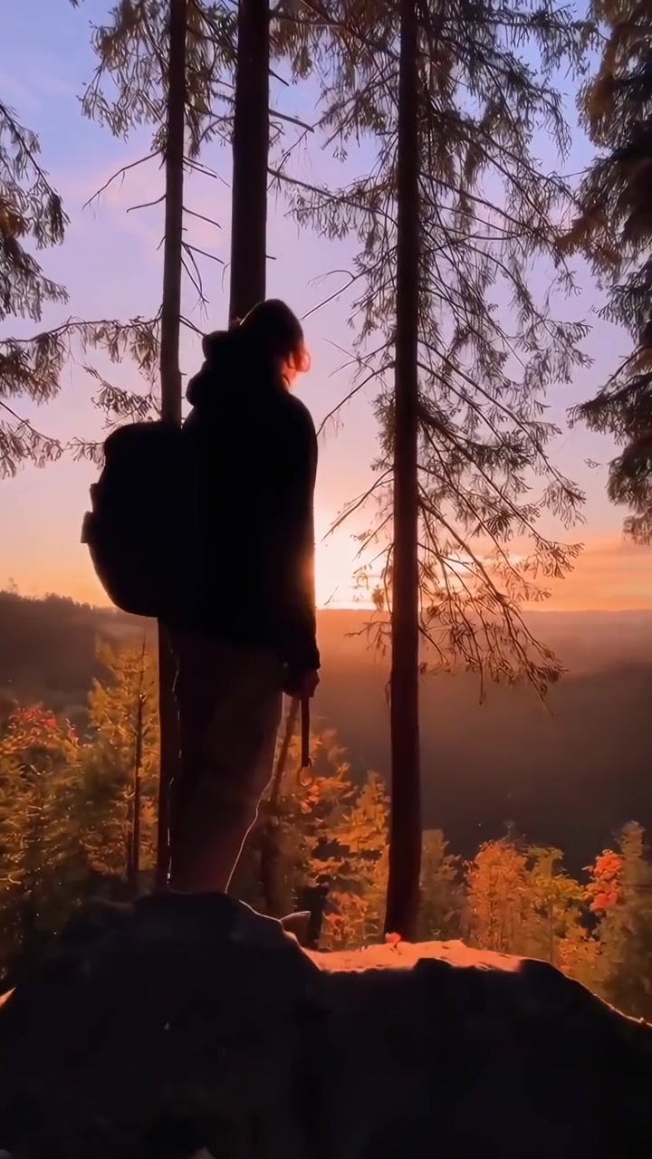 Hiker Standing on Rocky Cliff Overlooking Forest at Sunset