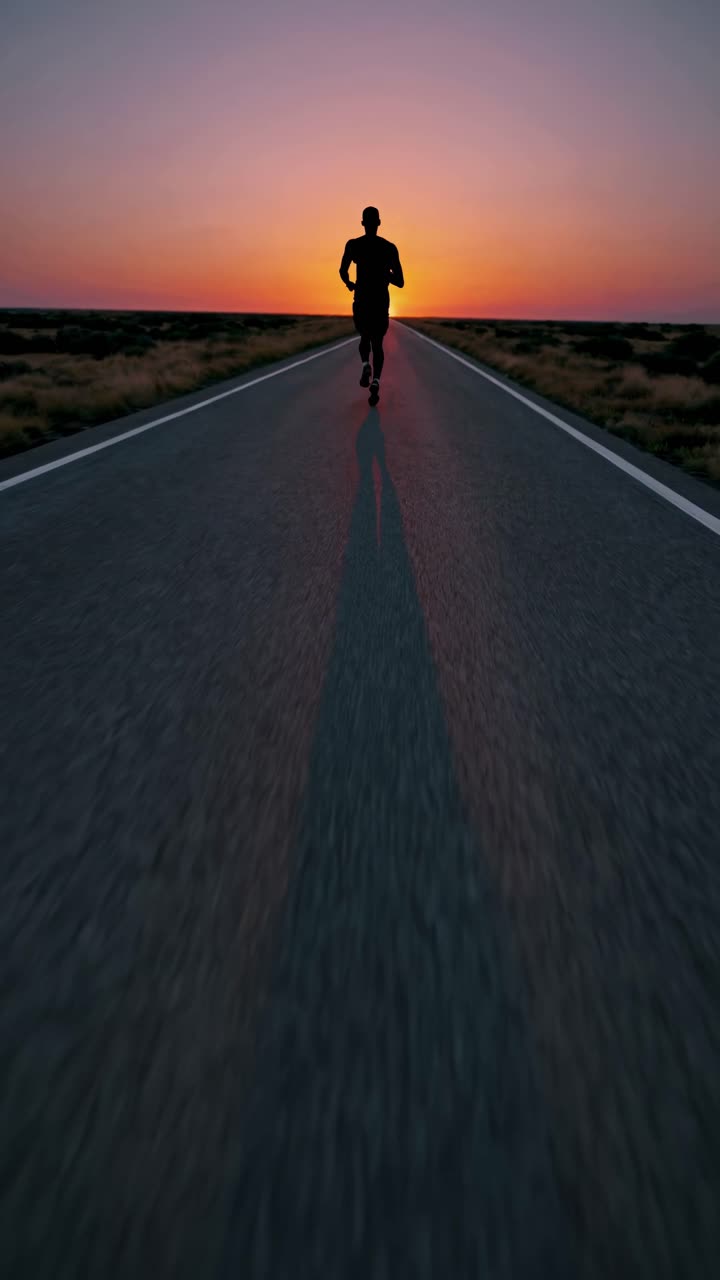 Silhouette of a person jogging on a road at sunset, captured from a low-angle, creating a dramatic