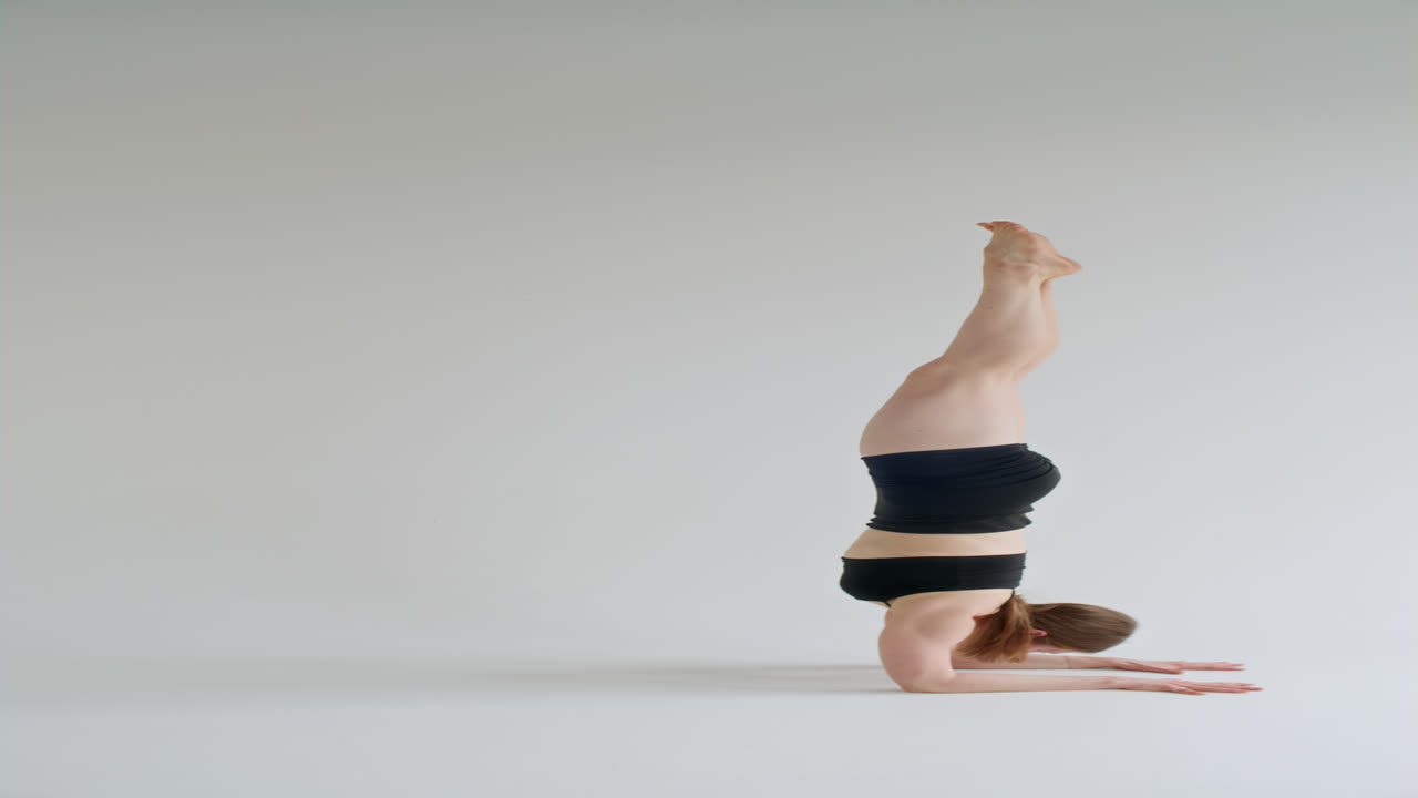 Nainen tasapainoilee Pincha Mayurasana -kyynärvarsiseisonnassa joogaharjoituksen aikana