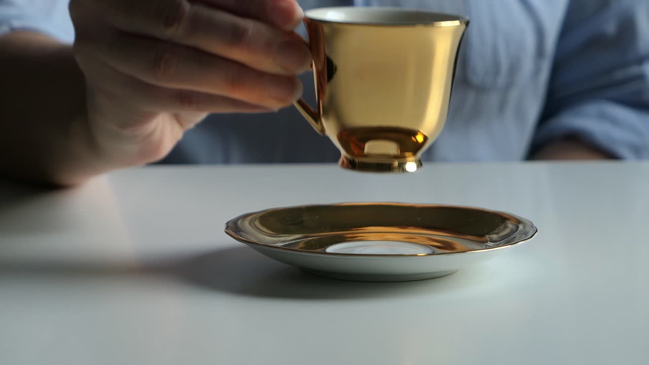Man waiter serving woman customer coffee from golden espresso cup, woman drinking coffee, close up