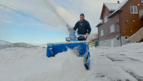 male removing snow in northern norway with a snow blower on a sunny day with great landscape in the background