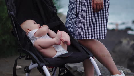 with the ocean as a backdrop, a young mother cherishes quality moments with her baby in the stroller, revealing her caring and devoted persona within this sweet family