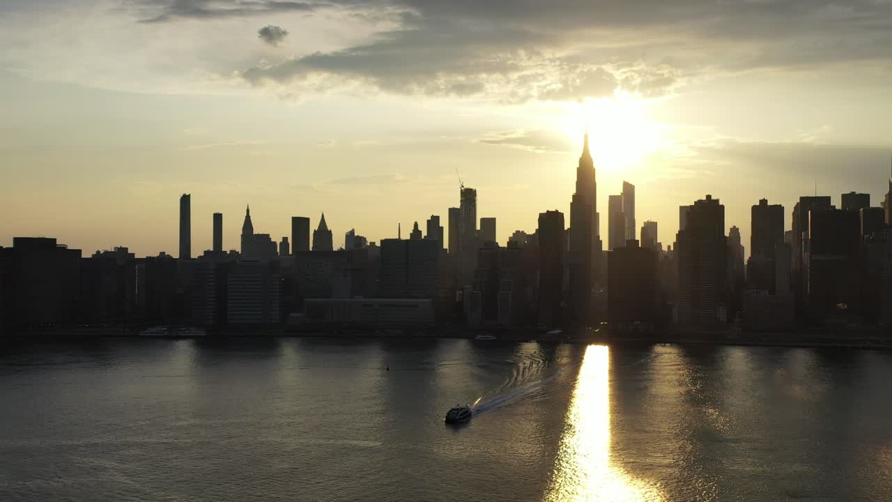 뉴욕시를 향해 앞으로 나아가는 돌리 샷 - 황금빛 일몰, 페리가 드론 카메라를 향해 움직일 때 강을 내려다보고 있습니다.