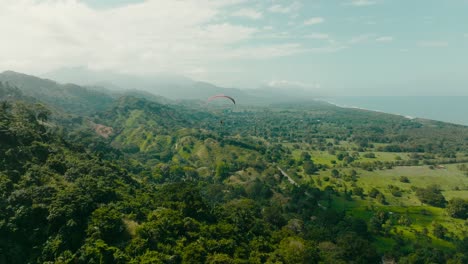 aerial shot chasing a paragliding flying towards the mountains and sea, colombia, la guajira