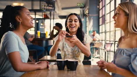 group of female friends meeting up in restaurant or coffee shop taking photo on mobile phone