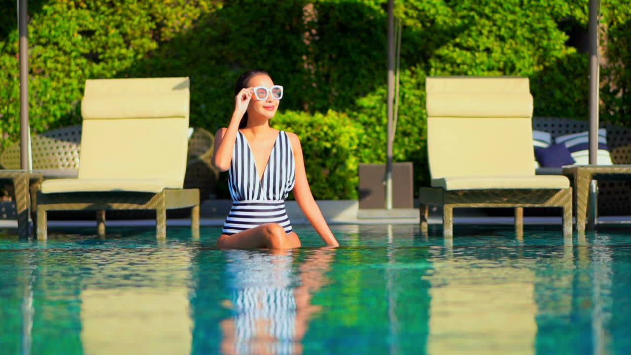 Charming Asian woman with black and white swimsuit sitting in pool water