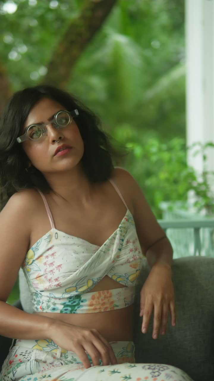 Relaxed young woman sitting indoors in summer outfit, looking away thoughtfully