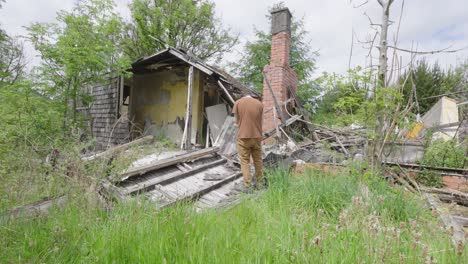 man surveys the aftermath of a storm and a destroyed house, handheld