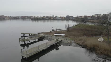 a scenic view of small wooden bridges on still water and people walking by on the sidewalk with the beautiful cityscape of karlskrona, sweden in the background