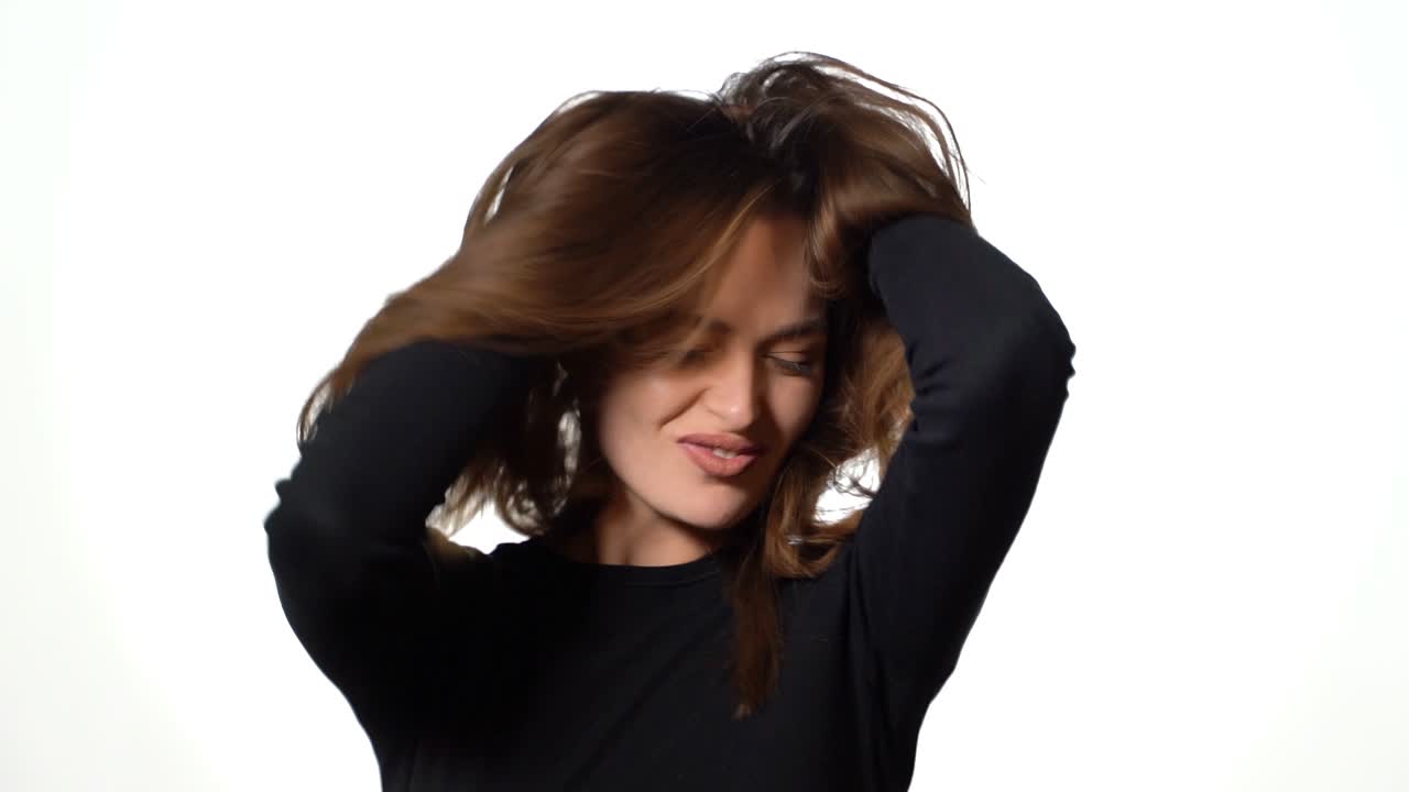 Happy brunette moves her hair and looks at camera. Attractive young girl on white background. Shaking her hair. Slow motion.