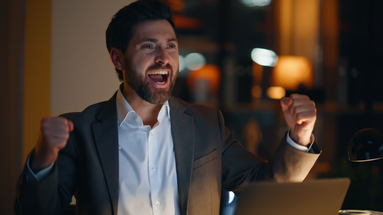 Primo piano di un vincitore emozionato che naviga sullo smartphone e fa un gesto di vittoria in ufficio di notte.