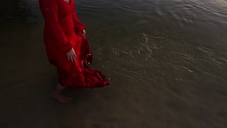 Close-up-tilt-up-gimbal-shot-of-woman-dropping-hem-of-her-dress-into-sea-water