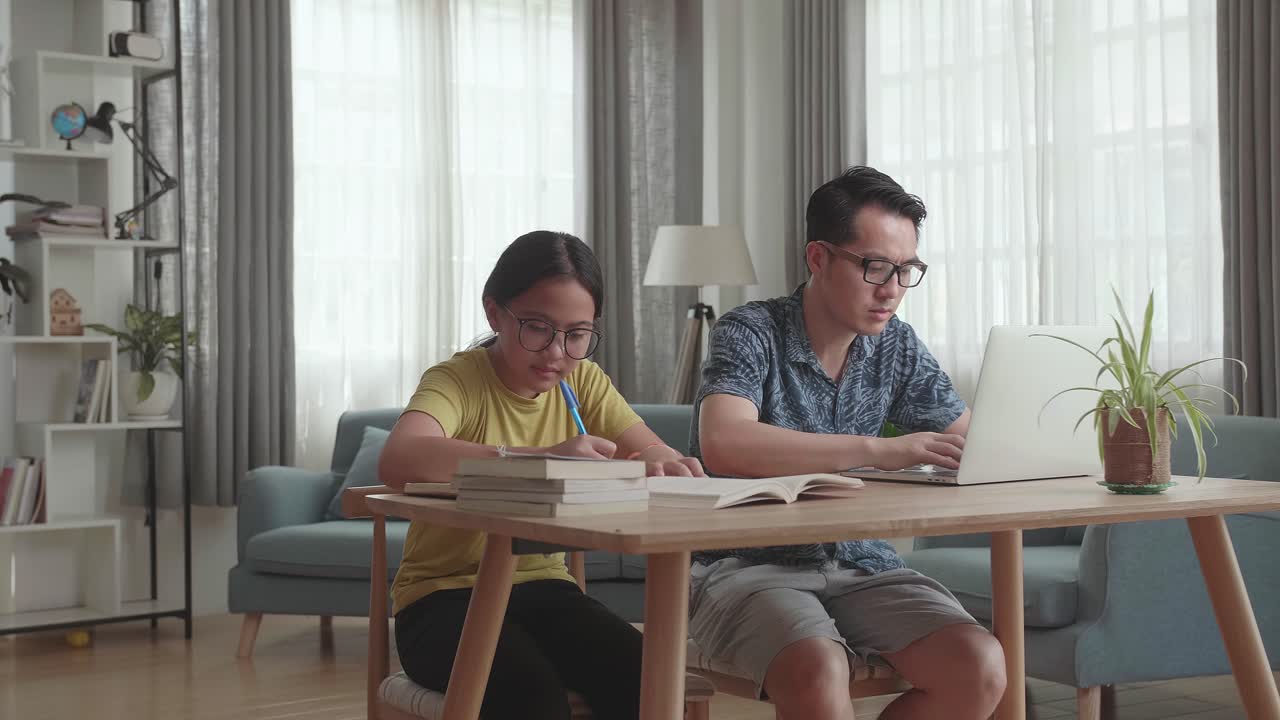 Asian Father Working With Laptop And Daughter Doing Homework At Living Room