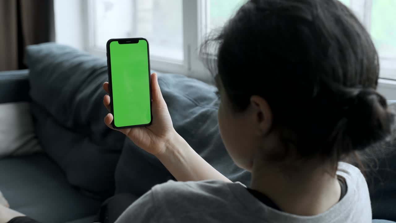 여성의 손은 녹색 화면의 스마트폰을 들고 소셜 네트워크, 영화, 비디오를 보고, 편안한 방의 소파에 누워 있습니다.