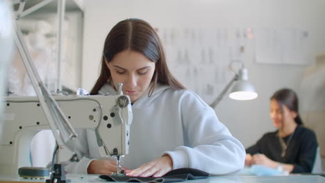 Die-Hände-Einer-Jungen-Frau-Sitzen-Und-Nähen-An-Der-Nähmaschine-Im-Kreativen-Designerstudio.-Zwei-Junge-Geschäftsfrauen,-Schneiderin,-Die-Neu-Macht