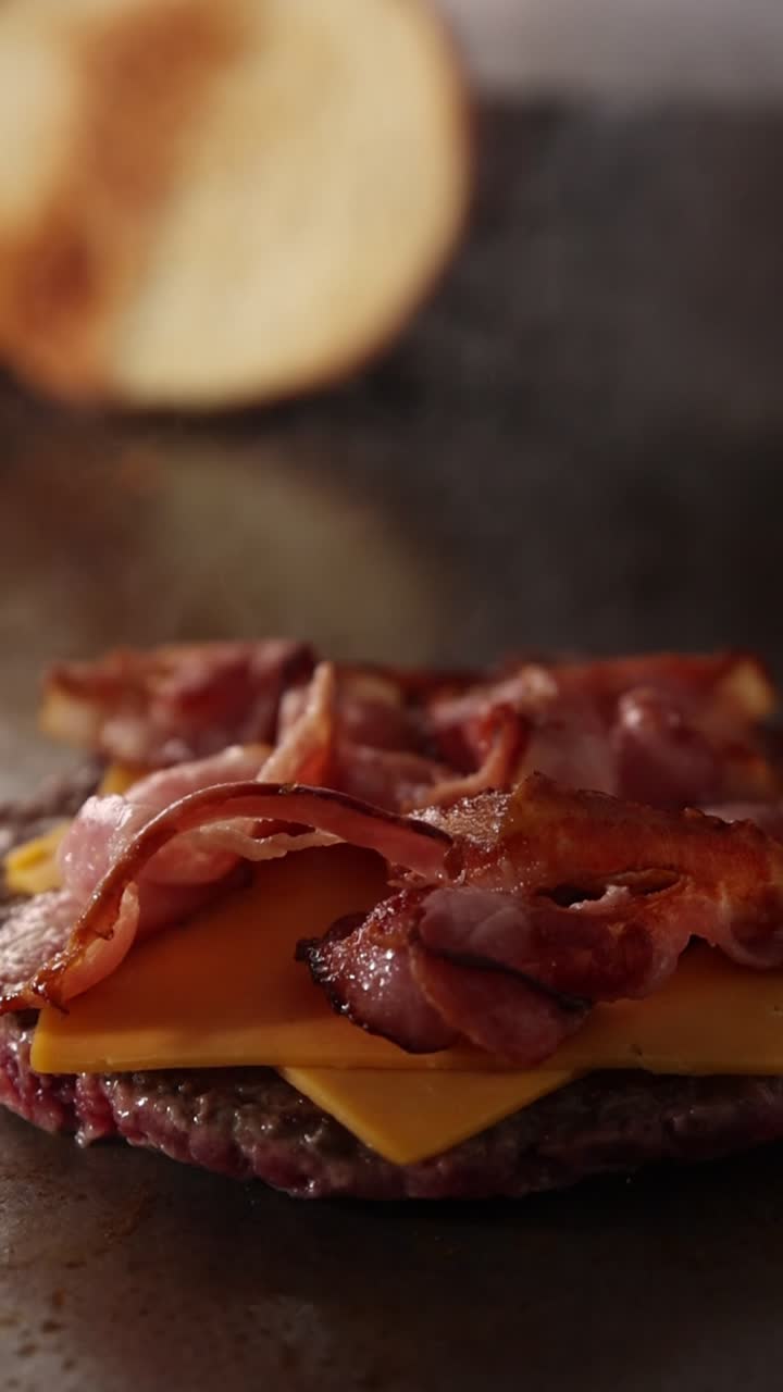 Chef che mette bacon e formaggio su un hamburger
