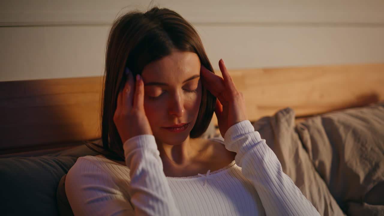 Primo piano di una donna che si soffia il naso che cola, tenendo un fazzoletto, sdraiata comodamente nel letto di casa