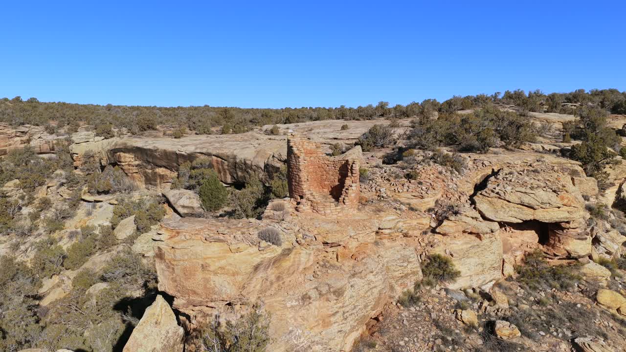 Uma antiga torre de alvenaria está situada em um penhasco de arenito dramático. Esta órbita de drone destaca a construção em pedra antiga e sua posição isolada dentro de uma região arborizada e acidentada de pinhões e juníperos