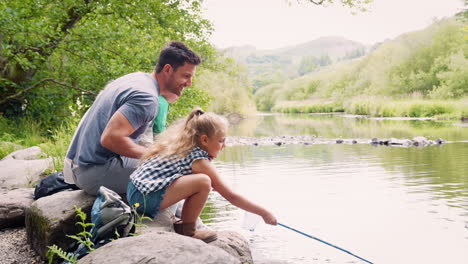 Zeitlupenaufnahme-Einer-Familie,-Die-Auf-Felsen-Sitzt-Und-Mit-Netzen-Im-Fluss-Im-Britischen-Seengebiet-Fischt