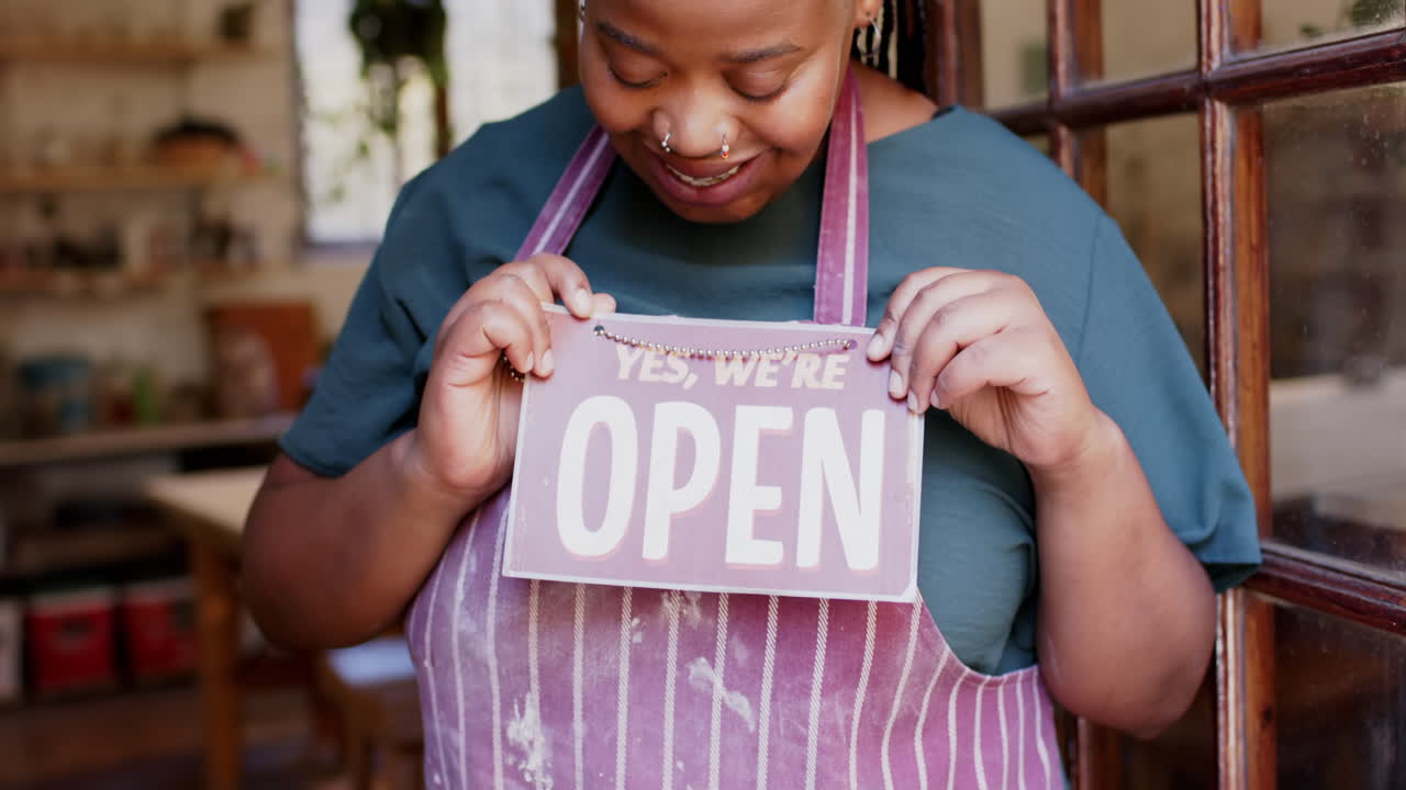 Happy african american female business owner holding shop sign to open and smiling, slow motion