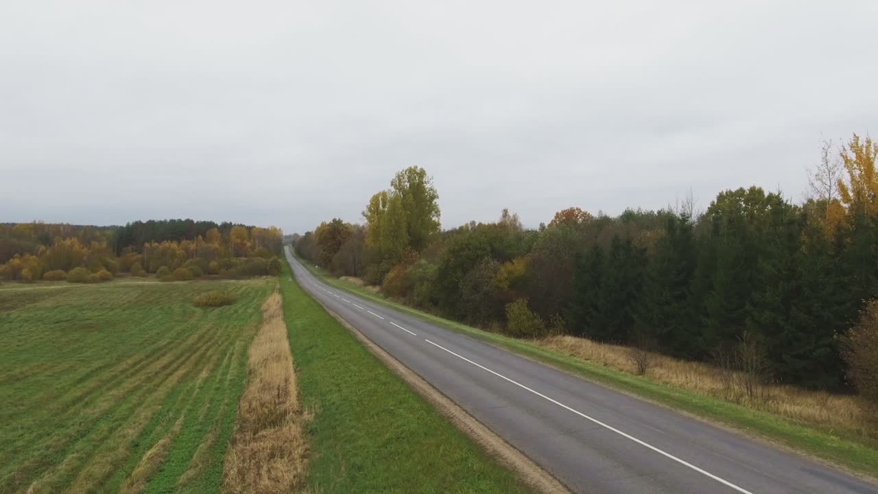 Regionální silnice vede zalesněnou krajinou v podzimním dni.