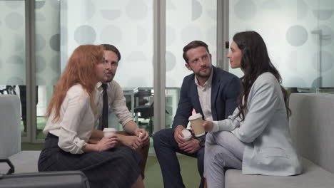 a working group of two businesswomen and two businessmen chatting relaxedly with some coffees in the lobby of an airport before a business trip 2