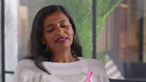 primer plano de una mujer madura que lleva una cinta rosa de concienciación sobre el cáncer de mama hablando en una reunión del grupo de apoyo de terapia para pacientes con tratamiento de cáncer