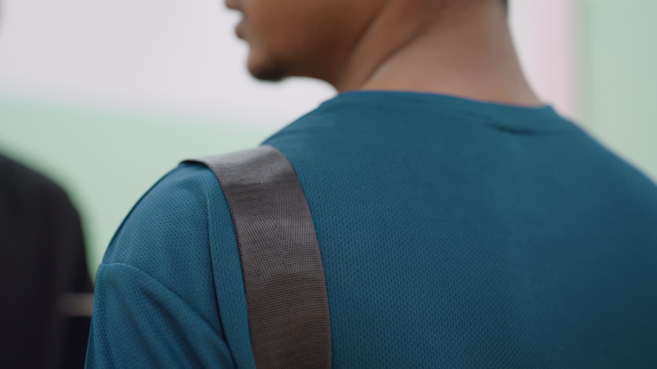 Close up of hand tapping man on shoulder indoors, focus on strap over blue shirt, capturing detail of supportive gesture and human interaction with soft blurred background