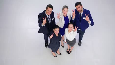 smiling businesspeople showing thumbs up and peace hand sign in office