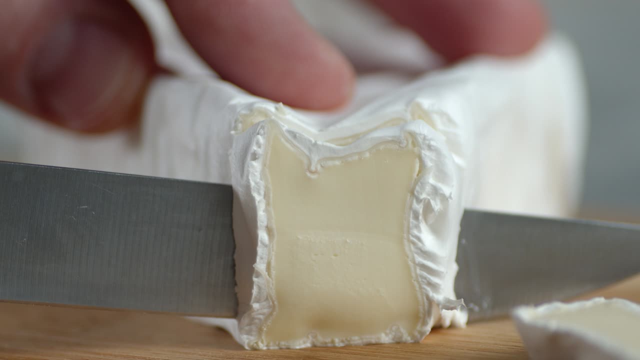 mano masculina con un cuchillo cortar pedazos de queso camembert.