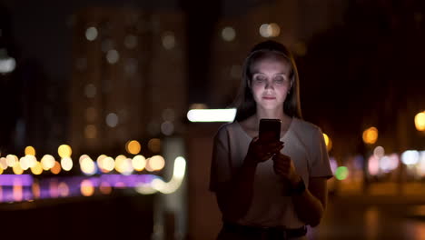 At-night-a-young-girl-sits-on-the-grass-in-a-big-city-and-looks-into-the-smartphone-screen-writes-a-message-and-maintains-her-personal-blog.