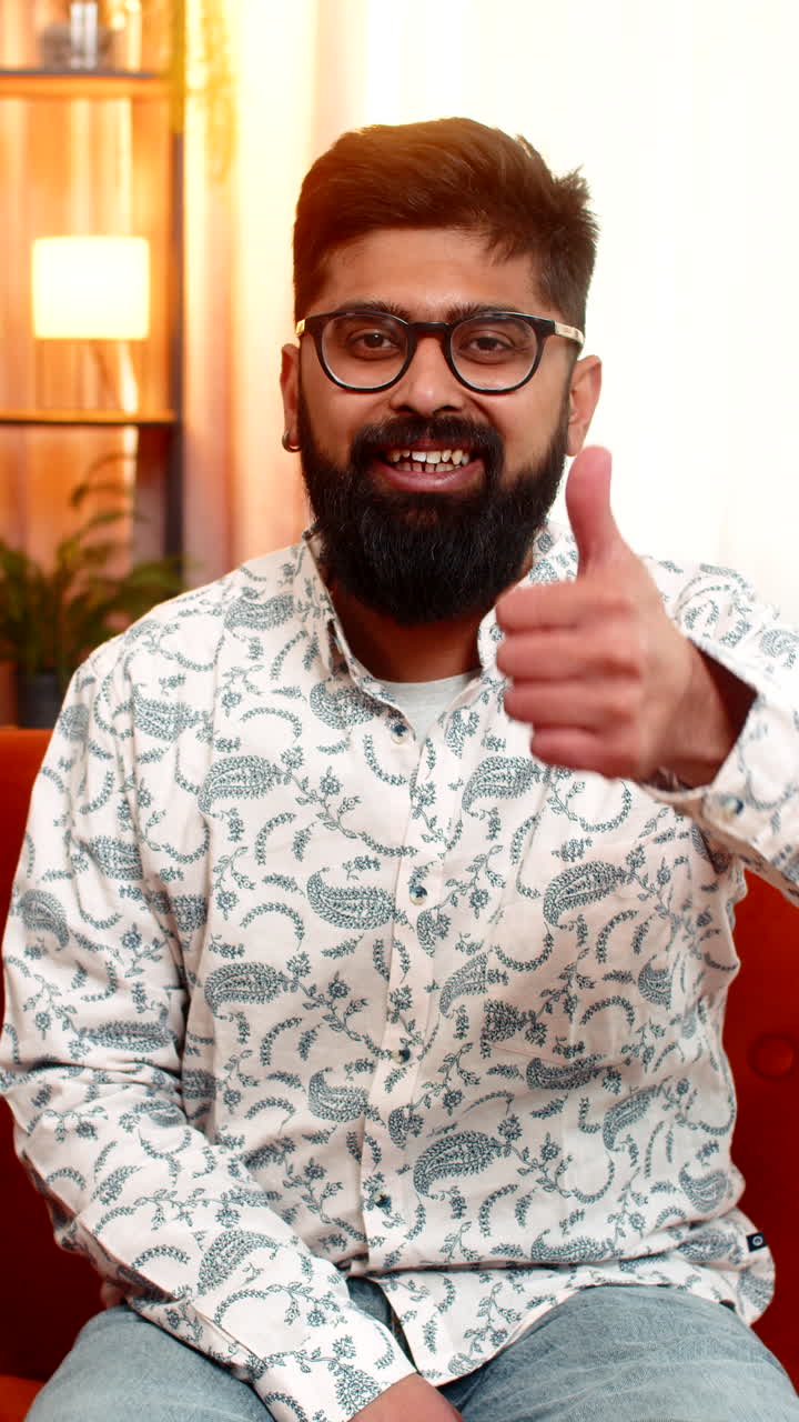 Indian man showing thumbs up with satisfied expression positive gesture of approval relaxing at home