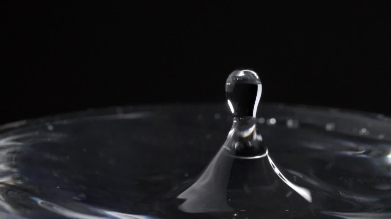 Water Droplets Splashing On Water Surface In Glass With Black Background, Close-Up