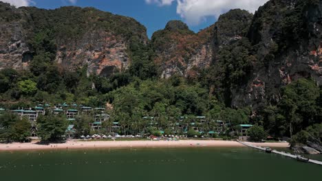 Moving-drone-view-of-a-town-situated-under-limestone-cliffs-at-Pai-Plong-Beach-in-Krabi,-Thailand