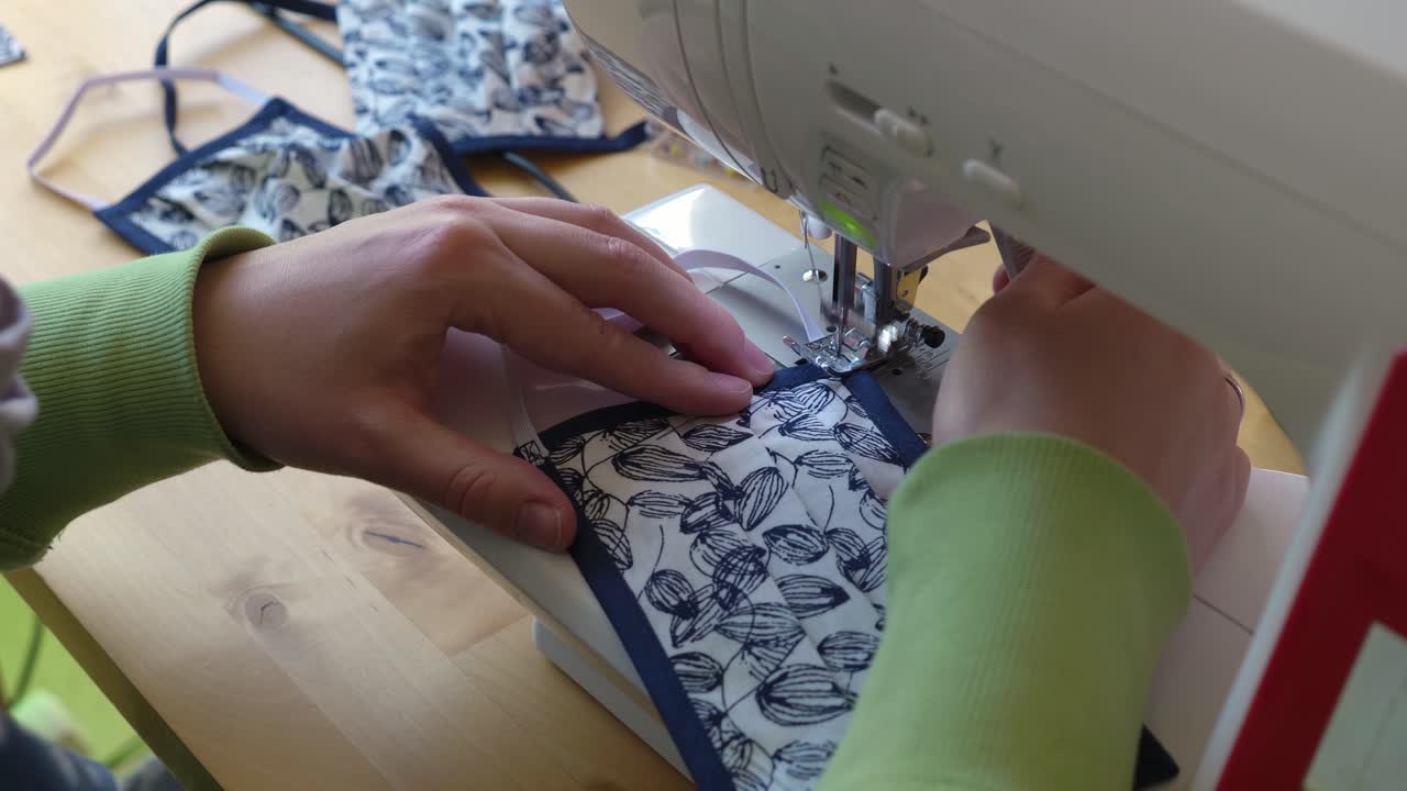 mujer cosiendo una banda de goma en una máscara facial con máscaras terminadas en el fondo