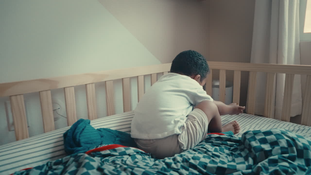 Black dad playfully wrestles toddler son in bed while baby brother watches. Joyful family moment showing laughter, bonding, and authentic parenting at home