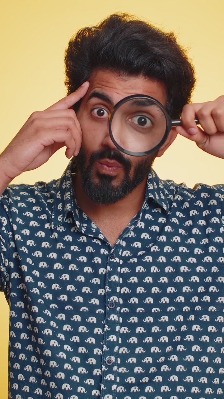 Investigator researcher man with magnifying glass near face looking into camera with big zoom eye
