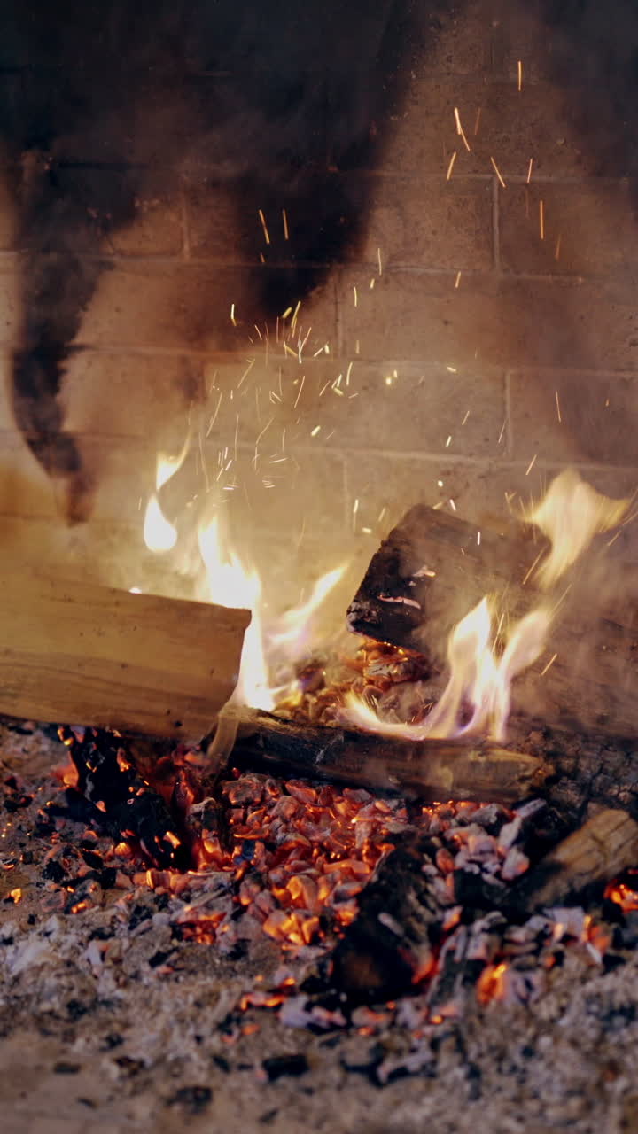 Male's hands split the heat with a log in the fire indoors. Close-up hands of a man putting wood into fire in fireplace and then warming up his cold hands. Christmas time. Vertical video