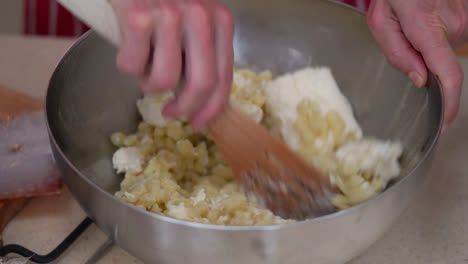 making bryndzove halusky. mixing bryndza (sheep milk cheese) into halusky (boiled lumps of potato dough) in a bowl. close up
