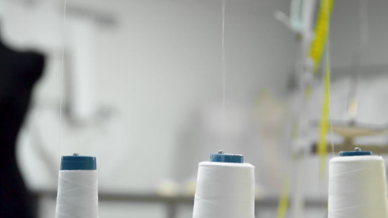 primer plano de tres grandes bobinas con hilo blanco delgado en una máquina de coser profesional en funcionamiento. imágenes de video en tiempo real en alta definición