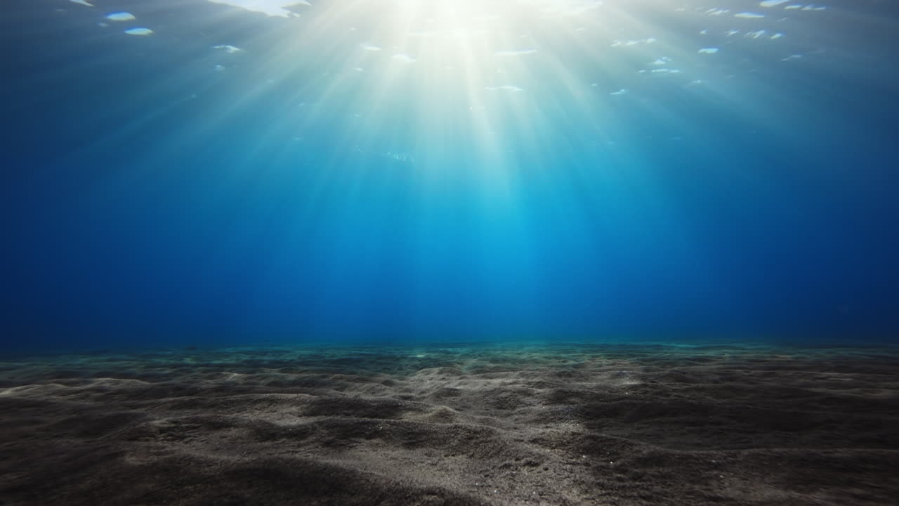 Sunlight filtering through clear blue ocean water onto a sandy seabed