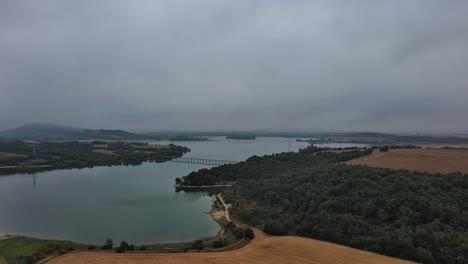 Overcast-view-of-Nanclares-de-Gamboa,-bridge-over-lake,-Basque-Country,-Spain,-aerial-shot