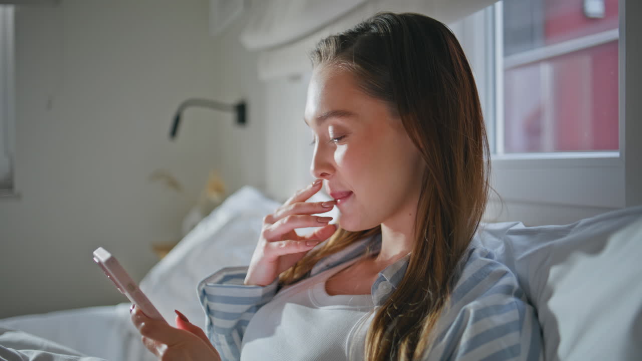 Ragazza gioiosa che guarda i contenuti dei social media sul telefono in camera da letto al primo piano al mattino