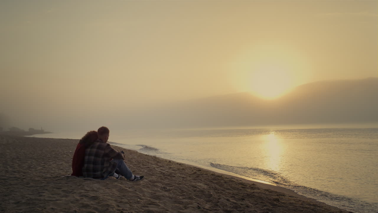 Loving couple sitting on sandy beach at ocean. Young lovers talking together