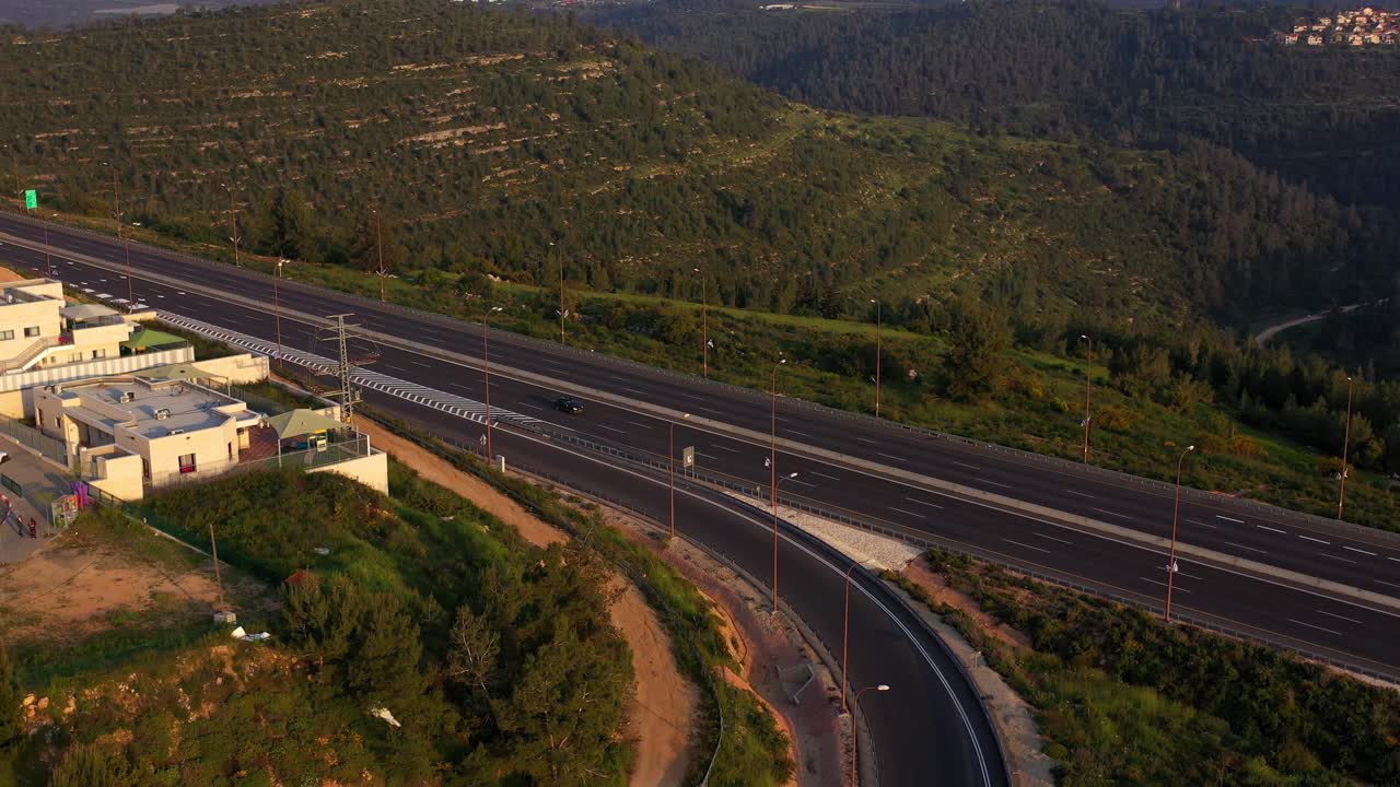 Aerial View of a Highway Winding Through a Green Mountainous Landscape at Golden Hour