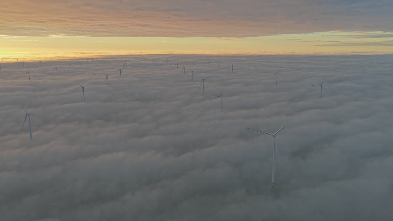 Havvindmøllepark lyser i solopgangen, vindmøller rejser sig gennem lave skyer.