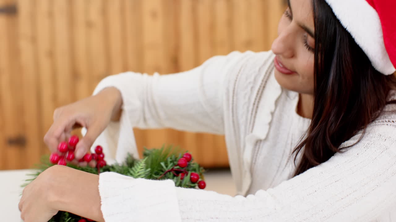 Indian woman decorating Christmas wreath with red berries, wearing Santa hat