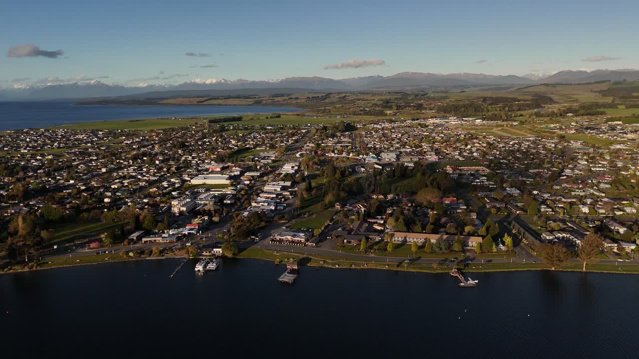 Cinematic backward aerial shot revealing the town of Te Anau and its stunning lake at sunset, located in the Fiordland region of New Zealand's South Island